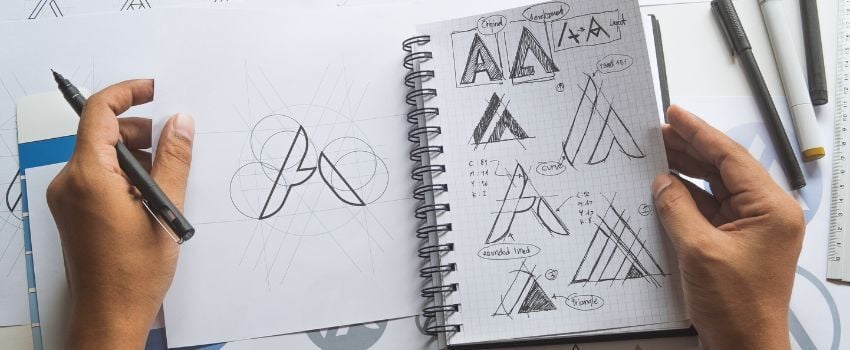 Manos trabajando en esbozos o borradores de diseños de un logo, siguiendo una serie de pasos de la guía de estilo de marca