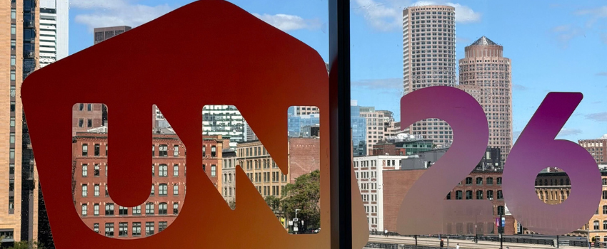 Instalación con el logotipo del evento UNBOUND 2026 recortado en el cristal de un ventanal, con el panorama urbano de Boston al fondo. 