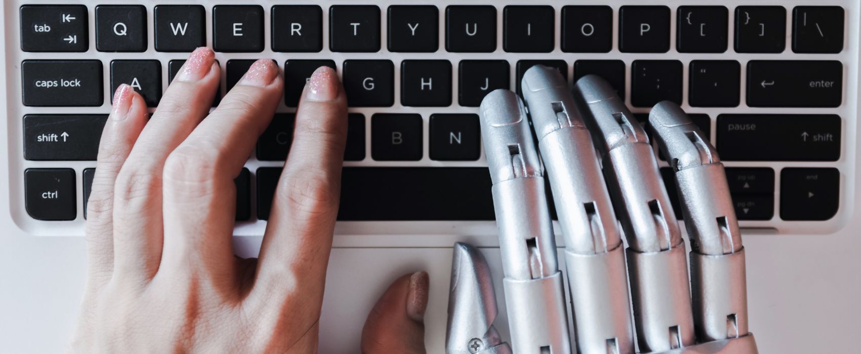 una mano humana y una mano robótica tecleando en una macbook