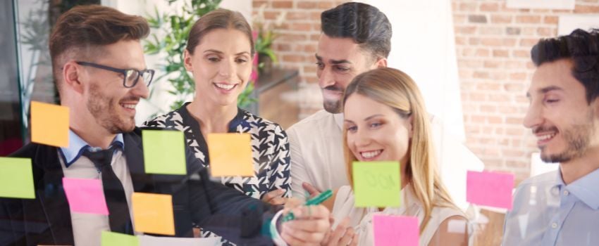Grupo de expertos en marketing de contenidos teniendo una dinámica presencial para generar ideas, trabajando con postits frente a un panel transparente