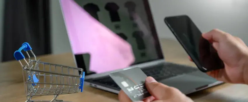 Usuario realizando compras en línea con una tarjeta de crédito frente a su laptop, lo que ilustra cómo funciona el e-commerce.